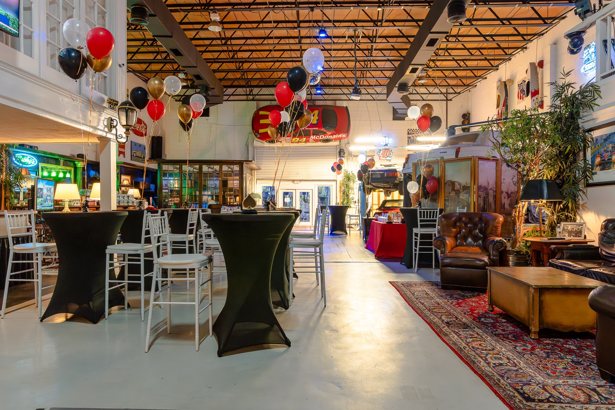 Wide view of the 51 Club auto shop set with cocktail tables and lounge seating beneath the exposed truss ceiling