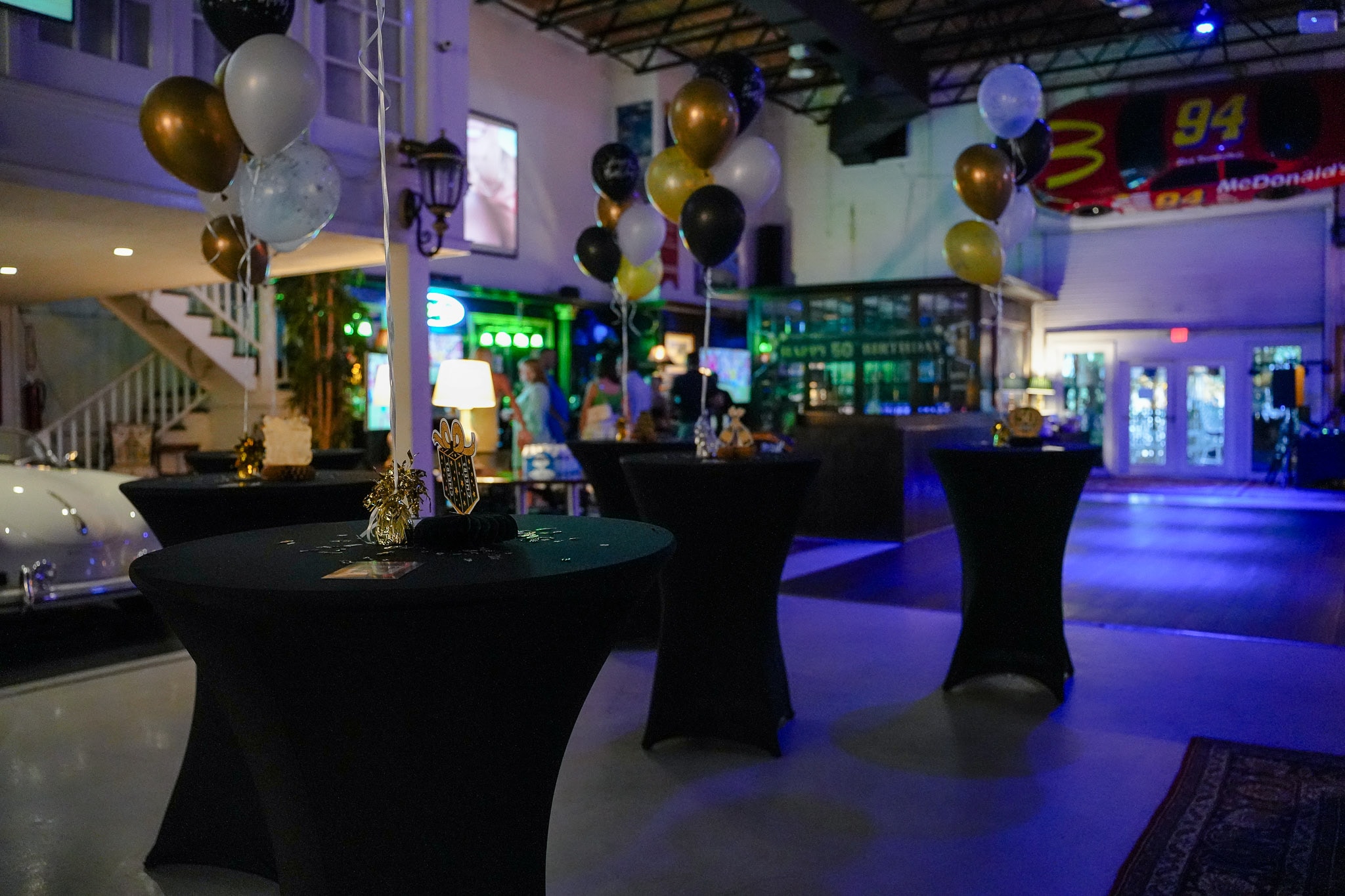 Cocktail tables with gold and black balloons set for an evening celebration